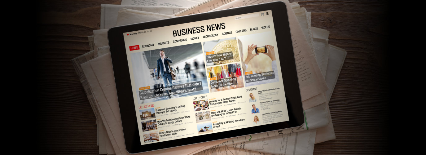 Tablet with business news website on stack of newspapers